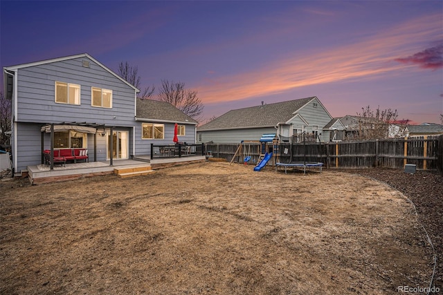 back of house featuring a trampoline, a playground, fence, and a wooden deck