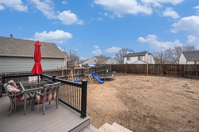 wooden deck featuring outdoor dining space, a trampoline, a playground, and a fenced backyard