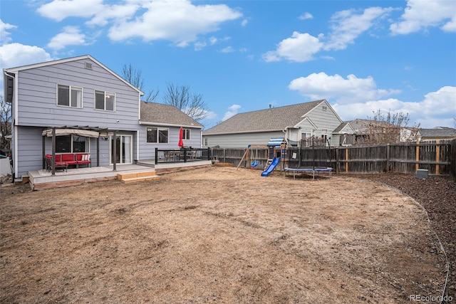 rear view of property with a trampoline, a fenced backyard, a playground, and a wooden deck