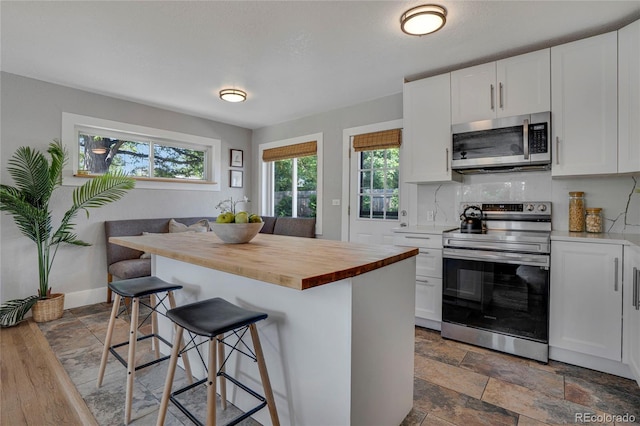 9400 Ridge Rd, Arvada, CO 80002 - kitchen featuring appliances with stainless steel finishes, wooden counters, a breakfast bar area, tasteful backsplash, and white cabinets