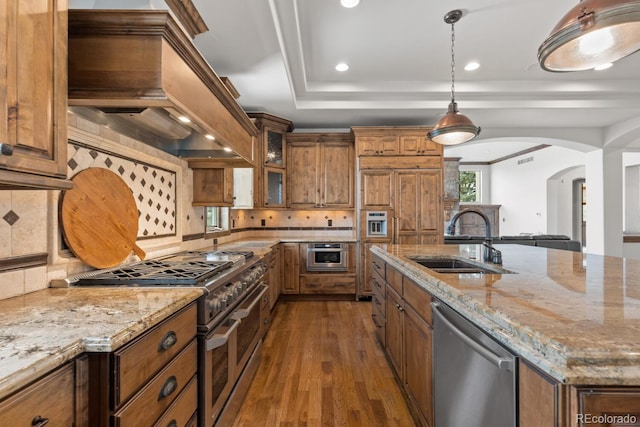 kitchen with premium range hood, appliances with stainless steel finishes, decorative light fixtures, sink, and light stone counters