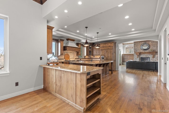 kitchen featuring decorative light fixtures, kitchen peninsula, a raised ceiling, and custom exhaust hood