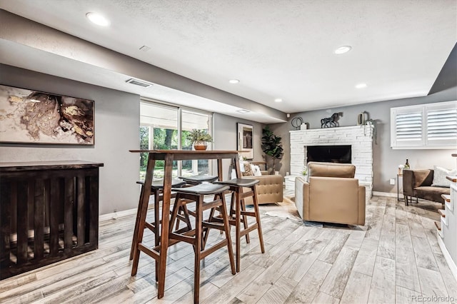 dining room featuring a textured ceiling, light wood-type flooring, and a brick fireplace