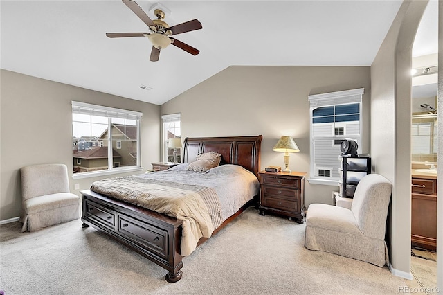 bedroom featuring ceiling fan, vaulted ceiling, light colored carpet, and ensuite bath