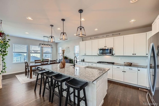 kitchen featuring hanging light fixtures, appliances with stainless steel finishes, a kitchen island with sink, and white cabinets