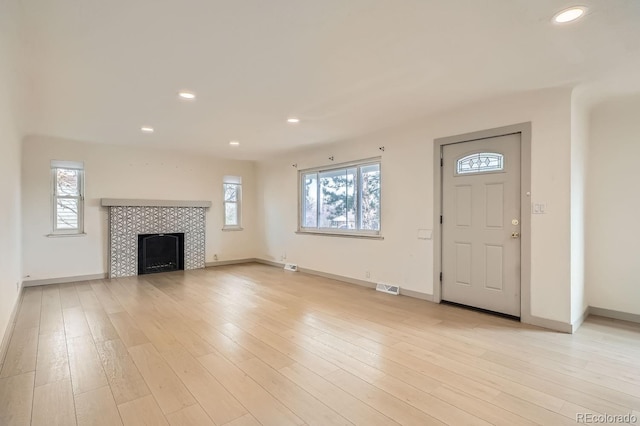 unfurnished living room featuring a tile fireplace, light wood-style flooring, and baseboards