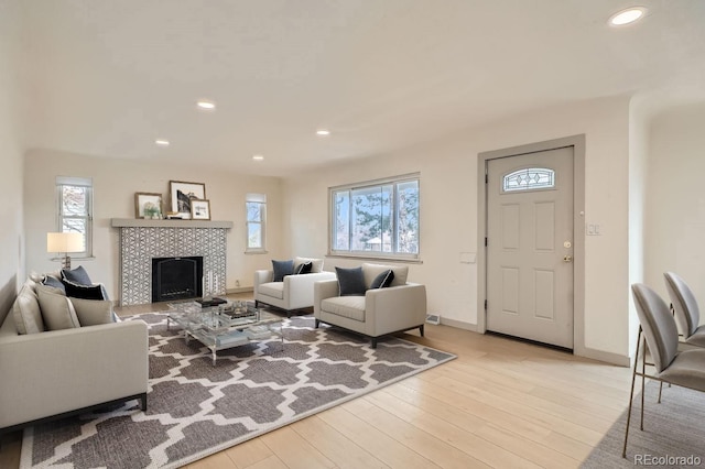 living room featuring light wood-type flooring, a fireplace, baseboards, and recessed lighting