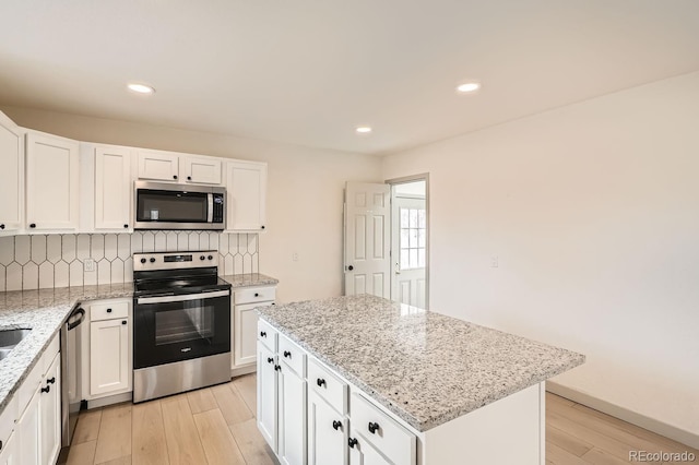 kitchen featuring stainless steel appliances, white cabinets, backsplash, and light wood finished floors