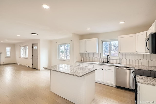 kitchen featuring tasteful backsplash, a center island, stainless steel appliances, light wood-style floors, and a sink