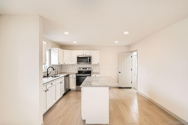 kitchen with light wood-style floors, a kitchen island, appliances with stainless steel finishes, and a sink