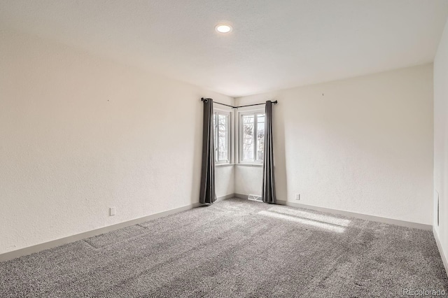 spare room with carpet, baseboards, and a textured wall