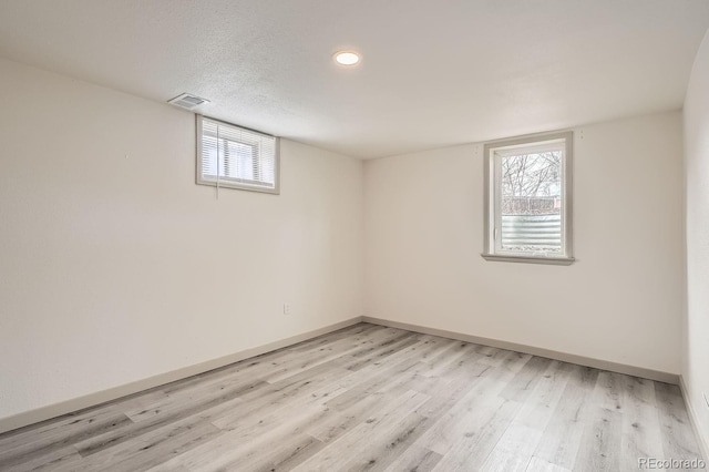 basement featuring light wood-style flooring, visible vents, baseboards, and a textured ceiling