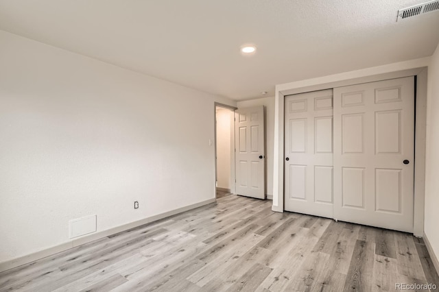 unfurnished bedroom featuring light wood finished floors, baseboards, visible vents, and a closet