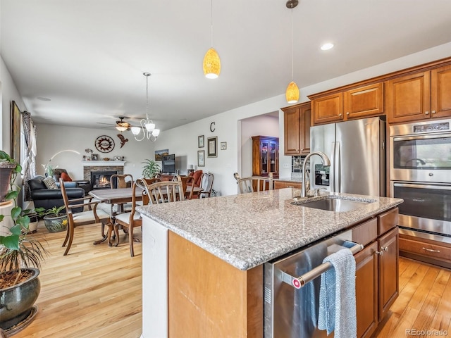 kitchen with an island with sink, open floor plan, stainless steel appliances, a stone fireplace, and pendant lighting