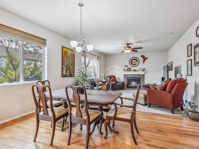 dining space featuring ceiling fan with notable chandelier, light wood-type flooring, a glass covered fireplace, and baseboards