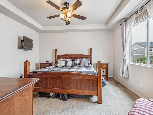 bedroom with light carpet, baseboards, a tray ceiling, and a ceiling fan