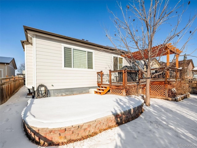 snow covered house with fence, a deck, and a pergola