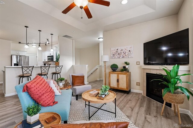 living room featuring visible vents, baseboards, light wood-type flooring, a raised ceiling, and a ceiling fan