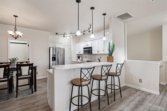 kitchen featuring visible vents, decorative backsplash, a peninsula, wood finished floors, and stainless steel appliances