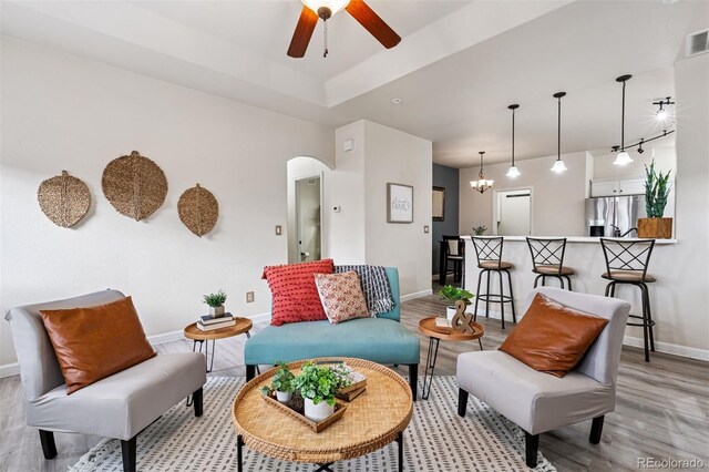 living room featuring a ceiling fan, baseboards, arched walkways, and light wood-type flooring