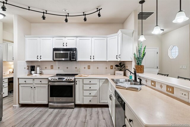 kitchen featuring appliances with stainless steel finishes, a sink, light countertops, a peninsula, and light wood-style flooring