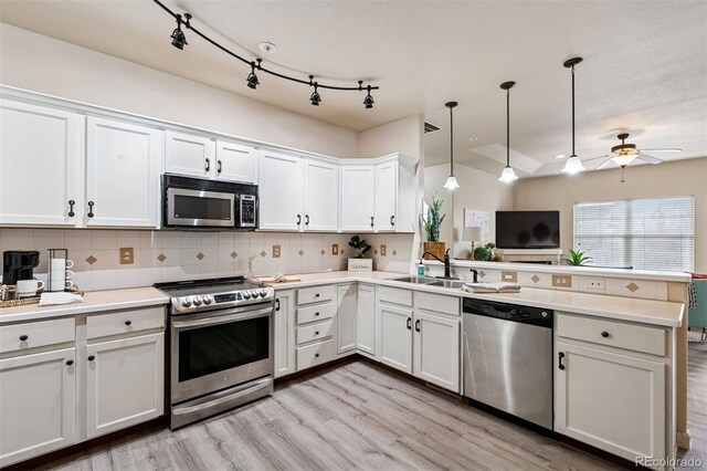 kitchen with decorative backsplash, a peninsula, white cabinets, a sink, and appliances with stainless steel finishes