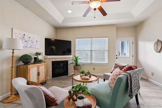 living area with baseboards, a ceiling fan, a tray ceiling, and light wood finished floors