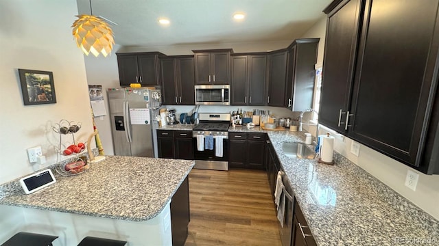 kitchen featuring dark brown cabinets, appliances with stainless steel finishes, wood finished floors, and light stone counters