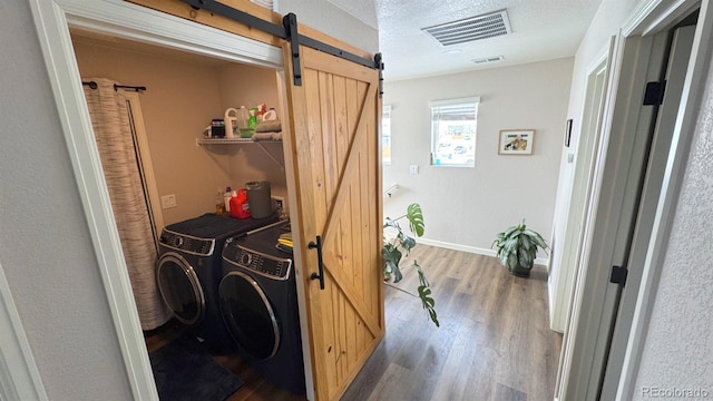 interior space with a barn door, washing machine and dryer, laundry area, wood finished floors, and visible vents