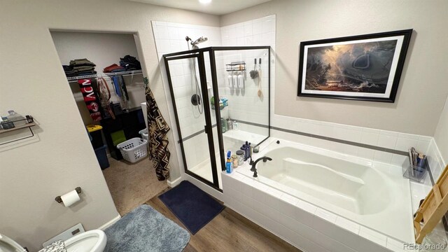 full bathroom featuring a walk in closet, a stall shower, a garden tub, and wood finished floors