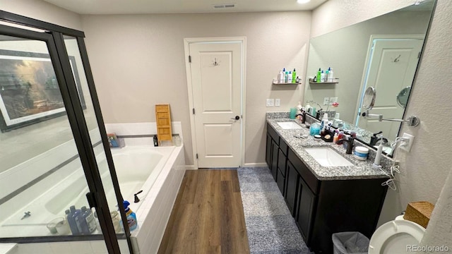 bathroom featuring double vanity, a garden tub, a sink, and wood finished floors