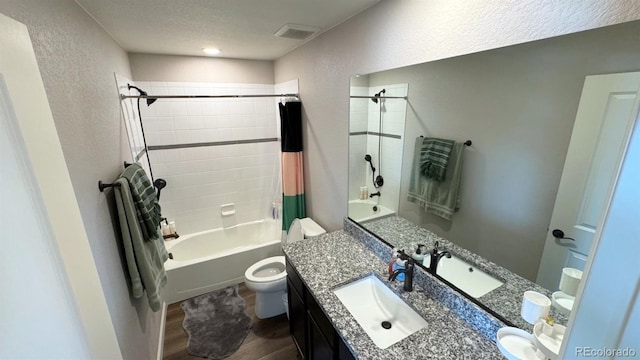 bathroom featuring visible vents, a textured wall, toilet, shower / bath combo with shower curtain, and vanity