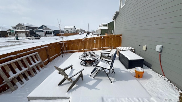 snow covered patio featuring a residential view, fence, and a fire pit