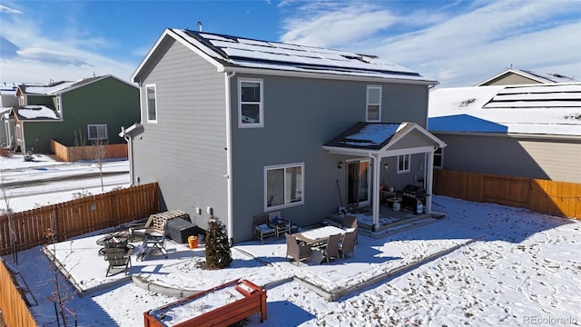 snow covered property featuring a fire pit, a patio, solar panels, and a fenced backyard