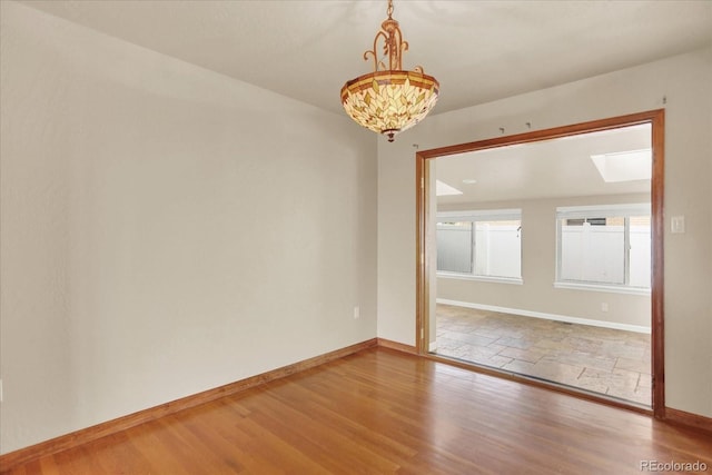 spare room featuring a skylight, baseboards, and wood finished floors
