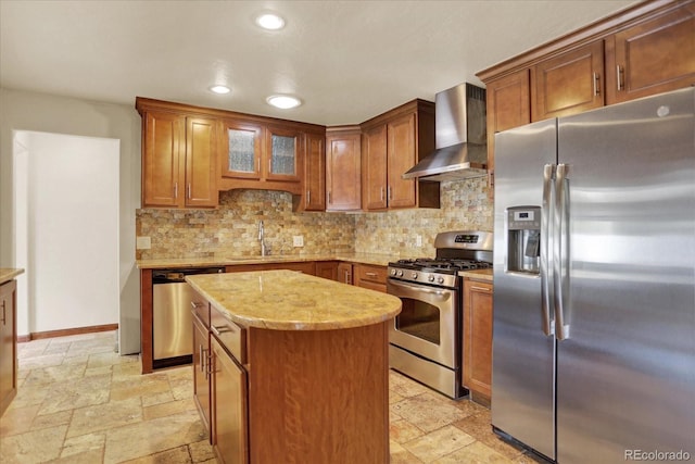 kitchen featuring stainless steel appliances, wall chimney range hood, a sink, stone tile floors, and recessed lighting