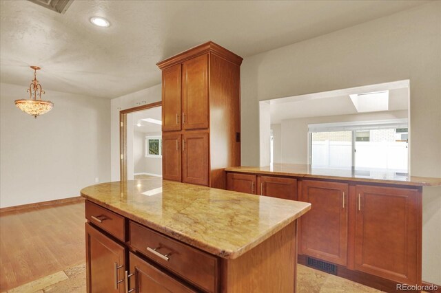 kitchen featuring a center island, light stone countertops, brown cabinets, decorative light fixtures, and a skylight