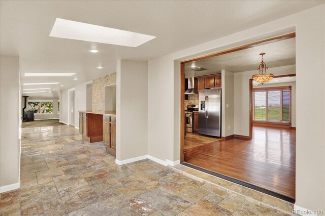 hallway with stone tile flooring, healthy amount of natural light, a skylight, baseboards, and recessed lighting