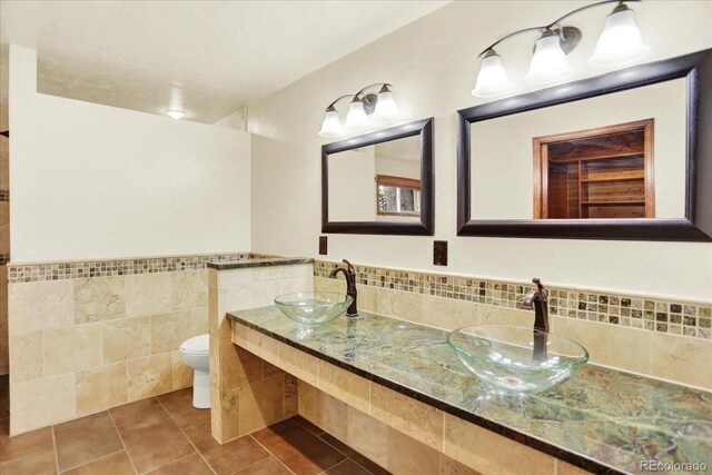 full bath with tile walls, tile patterned flooring, toilet, wainscoting, and double vanity