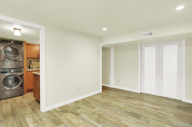 washroom with stacked washer and clothes dryer, cabinet space, light wood-style floors, baseboards, and recessed lighting