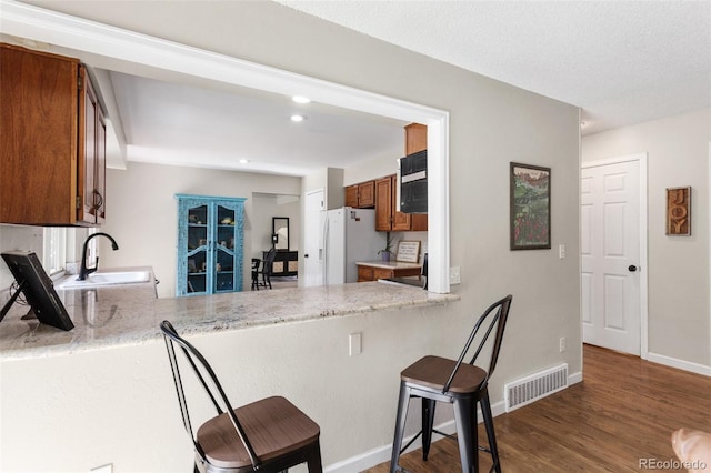 7951 S Webster Way, Littleton, CO 80128 - kitchen with white refrigerator with ice dispenser, brown cabinetry, dark wood-style flooring, a breakfast bar area, and a peninsula