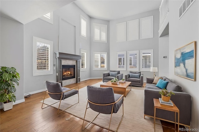 living room with a premium fireplace, a towering ceiling, a wealth of natural light, and light hardwood / wood-style flooring