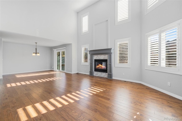 unfurnished living room with wood-type flooring, a tiled fireplace, and a high ceiling