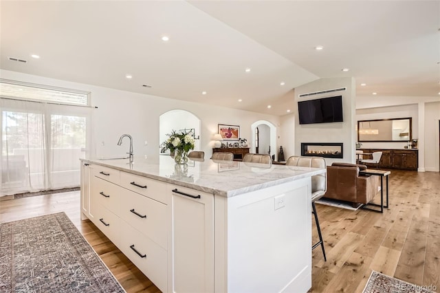 6102 S Aberdeen St, Littleton, CO 80120 - kitchen with a glass covered fireplace, a sink, white cabinets, light stone countertops, and light wood-style floors