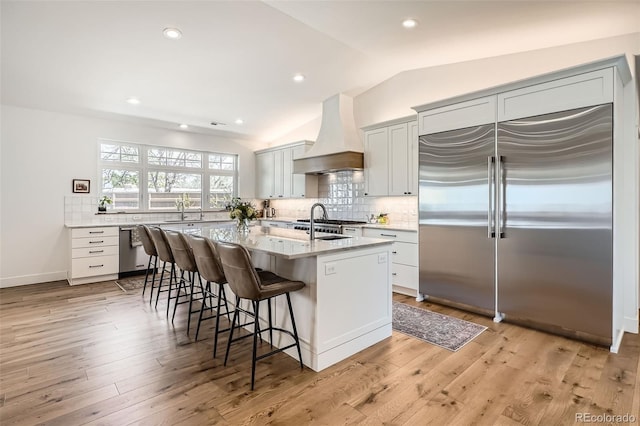 6102 S Aberdeen St, Littleton, CO 80120 - kitchen with appliances with stainless steel finishes, premium range hood, a breakfast bar area, a kitchen island with sink, and decorative backsplash