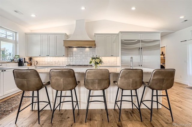 6102 S Aberdeen St, Littleton, CO 80120 - kitchen with premium range hood, vaulted ceiling, stainless steel appliances, backsplash, and a kitchen island with sink