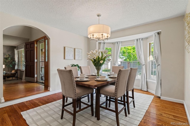 20922 E Crestline Cir, Centennial, CO 80015 - dining area with arched walkways, light wood finished floors, a chandelier, a textured ceiling, and baseboards