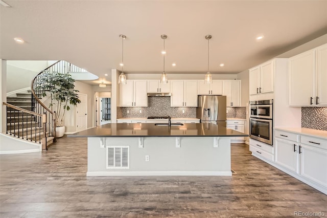 1715 Pioneer Cir, Lafayette, CO 80026 - kitchen with stainless steel appliances, a sink, dark countertops, a kitchen island with sink, and backsplash
