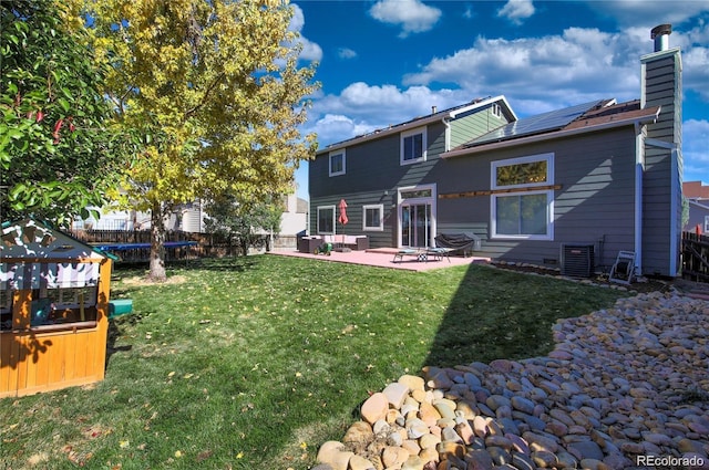 back of property with a yard, a patio, a chimney, roof mounted solar panels, and fence