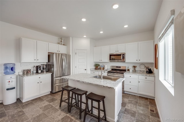 kitchen with stainless steel appliances, a sink, stone finish floors, white cabinets, and a kitchen bar